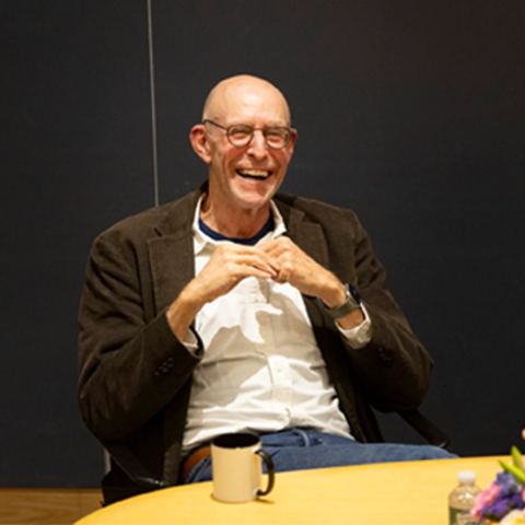 Michael Pollan, laughing, sitting at a table while lecturing