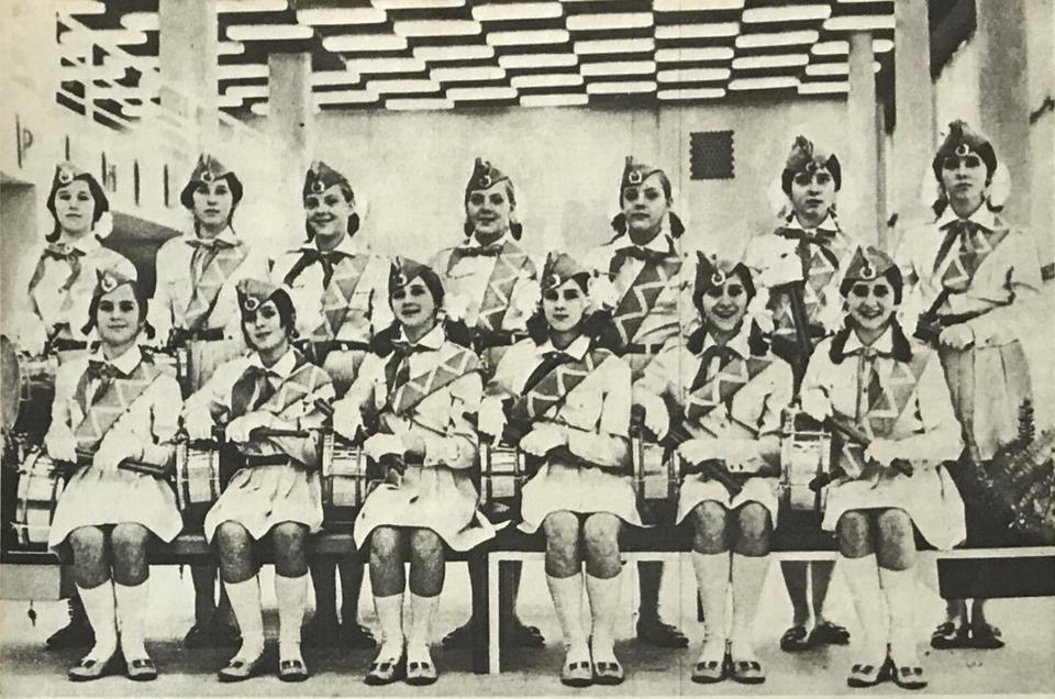 Thirteen young female drummers in uniform.