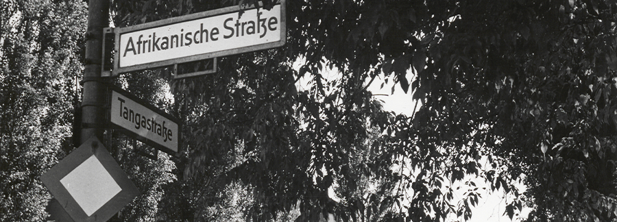 Black and white photo of street signs at a corner, reading 